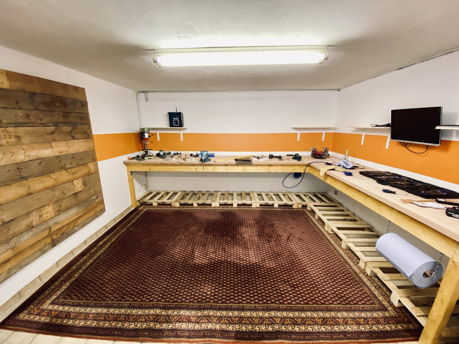 Blick auf die Werkbank mit Standbohrmaschine, Schraubstock und Ablagen